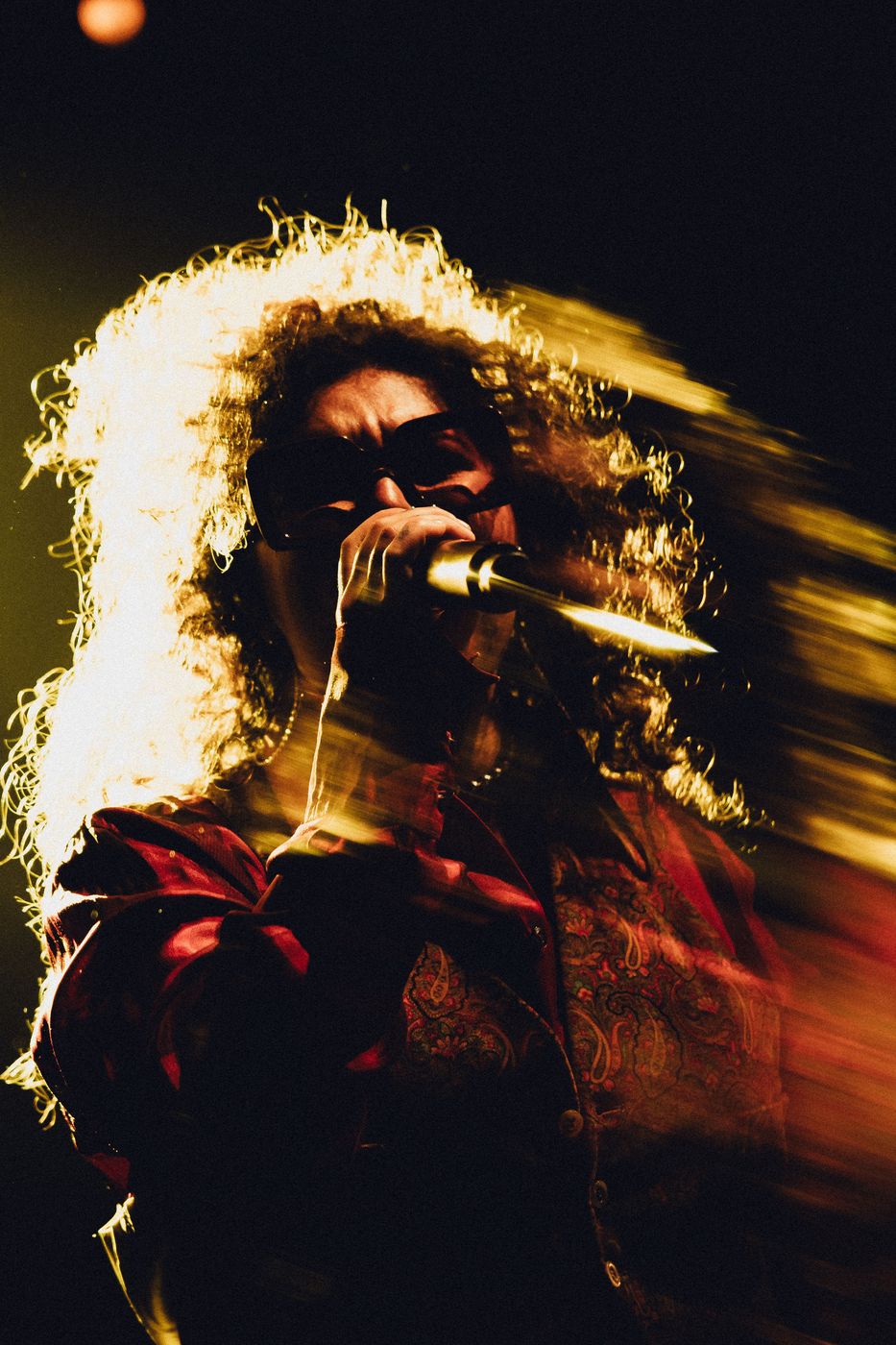 Singer in sunglasses performing under warm stage lighting