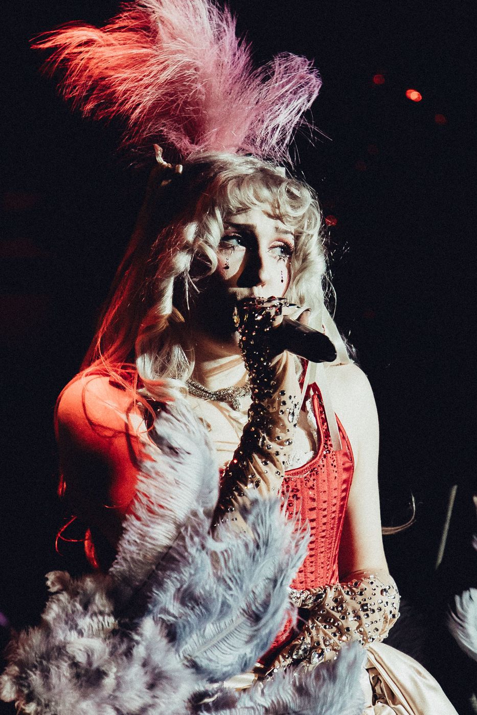 Vintage-styled performer with a feather headdress under red stage light