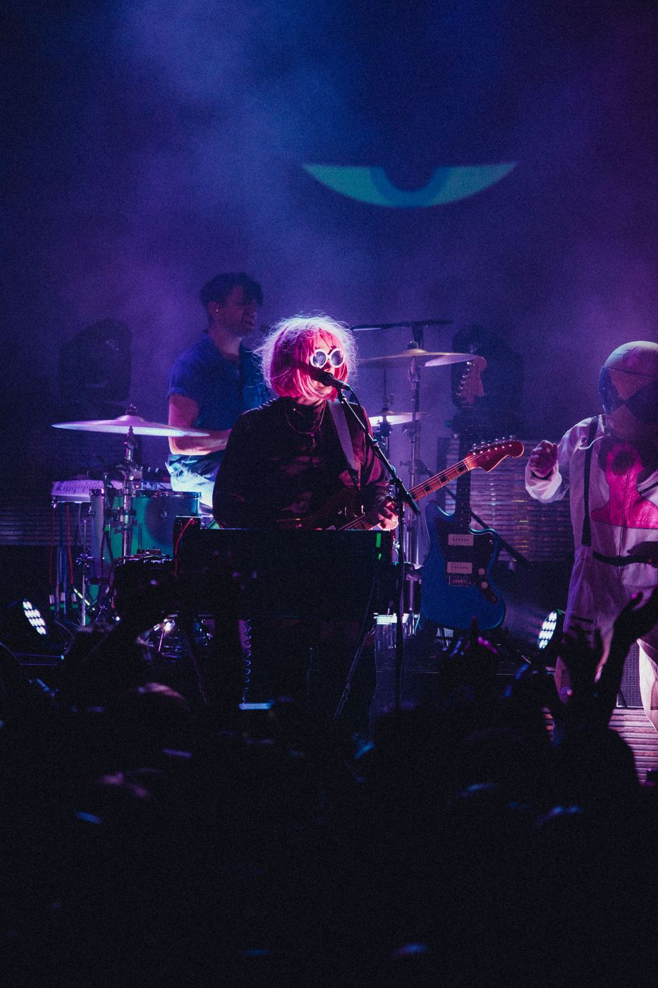 Performer in pink wig and sunglasses on stage beside a costumed bandmate