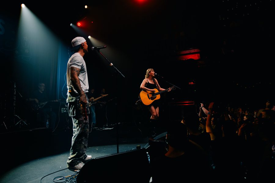Two performers singing together onstage under concert lighting
